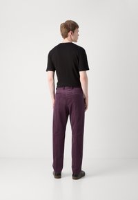 T-shirt noir à manches courtes associé à un pantalon violet, doté d'une coupe droite et d'un design minimaliste. Les chaussures sont noires avec une semelle marron.
