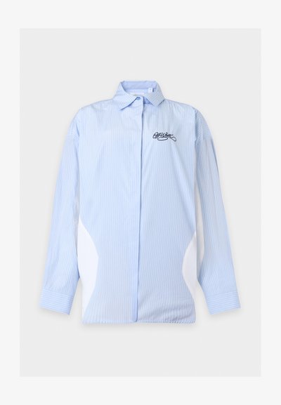 Chemise bleu clair à manches longues avec fines rayures verticales, col classique, panneaux latéraux blancs et petit logo brodé sur la poitrine gauche.