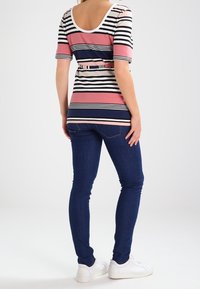 Randig topp i rosa, marinblå och krämfärgad; kort ärm; bälte i midjan. Matchas med mörkblå tajta jeans och vita sneakers. Bakvy.