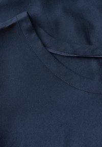 Le tissu en coton bleu marine présente une texture lisse, avec un col rond et des détails de couture subtils. Design simple et classique.