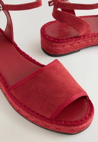Rode suède sandalen met een open teen, enkelbandje en geweven jute details op de zool. Platte zwarte rubberen buitenzool voor grip.