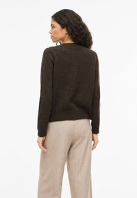 Brun strikkegenser med lange ermer og rund hals, kombinert med lysebeige bukser, som viser en teksturert stoff og avslappet passform.