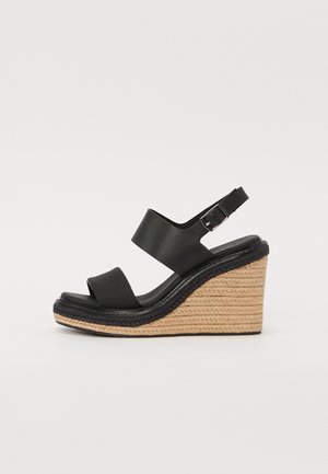 Sandale compensée noire avec deux larges brides, une bride réglable avec boucle et une semelle plate-forme en jute tressé.