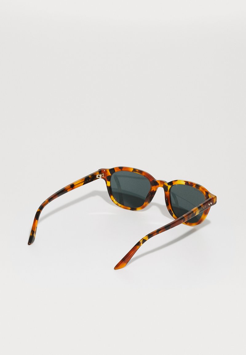 Tortoiseshell zonnebril met donkere lenzen, ovale montuur en slanke armen die een gemengd bruin en gele patroon tonen.