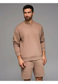 Felpa in cotone marrone chiaro con collo rotondo e polsini a costine, abbinata a pantaloni corti coordinati, caratterizzata da un design semplice e linee pulite.