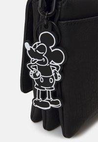 Schwarze Kunstledertasche mit strukturierter Oberfläche; verfügt über einen schwarz-weißen Mickey Mouse Schlüsselanhänger, der am Reißverschluss befestigt ist.