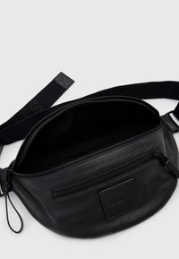 Zwarte leren heuptas met een ritssluiting hoofdcompartiment, een extra voorvak en een verstelbare band met logo-detail.