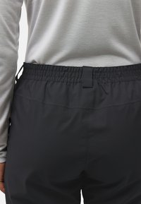 Person trägt schwarze elastische Bundhose und ein hellgraues Langarmshirt, von hinten in Taillenhöhe gezeigt.