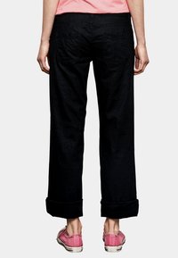 Zwarte wijde cropped broek met opgerolde zomen, voorzien van achterzakken. Gemaakt met roze canvas schoenen, wat een casual stijl weergeeft.