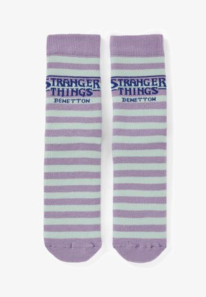 Calcetines hasta la rodilla a rayas en lavanda y verde menta, con los logotipos "Stranger Things" y "Benetton" en tejido azul en la parte superior.