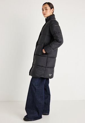 Czarny puchowy płaszcz z wysokim kołnierzem, bocznymi kieszeniami i poziomym pikowaniem. Połączony z szerokimi dżinsami.