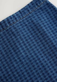 Blauer Denim-Stoff mit einem strukturierten Muster aus kleinen Rauten und einer kontrastierenden goldenen Naht entlang der oberen Kante.