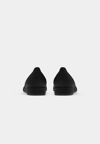 Black flat shoes with a smooth texture, pointed toe design, minimal heel, and subtle stitching detail at the back and sides.