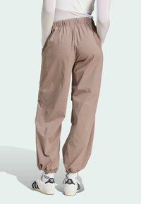 Lightweight, beige jogger pants with elastic waistband and cuffs, featuring side pockets and a smooth texture. Paired with white sneakers.