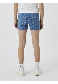 Shorts en denim avec un délavage bleu clair et un motif de papillons ; dotés de deux poches arrière et d'un ourlet effiloché ; portés avec des chaussettes blanches et des baskets.