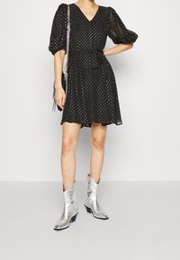 Black short dress with puff sleeves, polka dot pattern, tying waist belt, paired with shiny silver cowboy boots.
