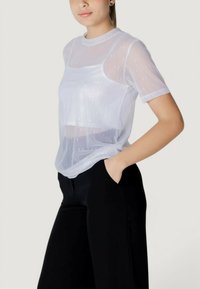 Camiseta blanca transparente de manga corta, con un patrón sutil. Combinada con pantalones negros, tiene un corte relajado y un escote redondeado.