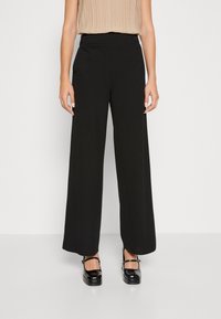 Pantalons larges noirs avec une taille haute, dotés de deux boutons à l'avant. Tissu lisse avec une silhouette fluide.