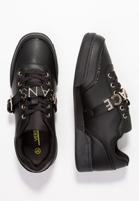 Baskets noires avec détail du logo métallique, dotées d'une tige en cuir lisse, de laçage et d'une semelle en caoutchouc avec adhérence texturée.