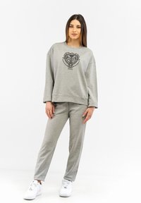 Grey sweatshirt with graphic logo on the front, paired with matching grey sweatpants. Model wears white sneakers. Smooth fabric texture.