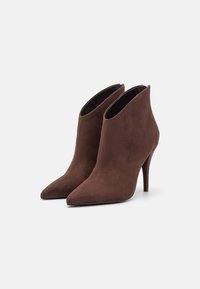 Stivaletti alla caviglia in suede marrone con punta affilata e tacco stiletto sottile. Presentano un design con lato aperto e dettagli di cucitura minimal.