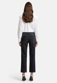 Czarne dżinsy o prostych nogawkach z dwoma tylnymi kieszeniami, zestawione z białą koszulą na guziki. Materiał ma gładką fakturę i minimalne zdobienia.