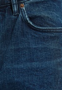 Jeans de mezclilla azul oscuro con un diseño clásico de cinco bolsillos, que presentan un detalle de remache de cobre y costuras visibles a lo largo de los bordes.