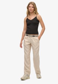 Camisola nera con bordo in pizzo abbinata a pantaloni di lino beige. I pantaloni hanno una vita elasticizzata con un accento di marca. Design leggero e casual.