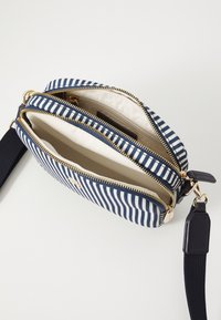 Borsa a tracolla in tessuto a righe blu e bianco, con zip dorate, due scomparti e una tracolla blu staccabile per maggiore versatilità.
