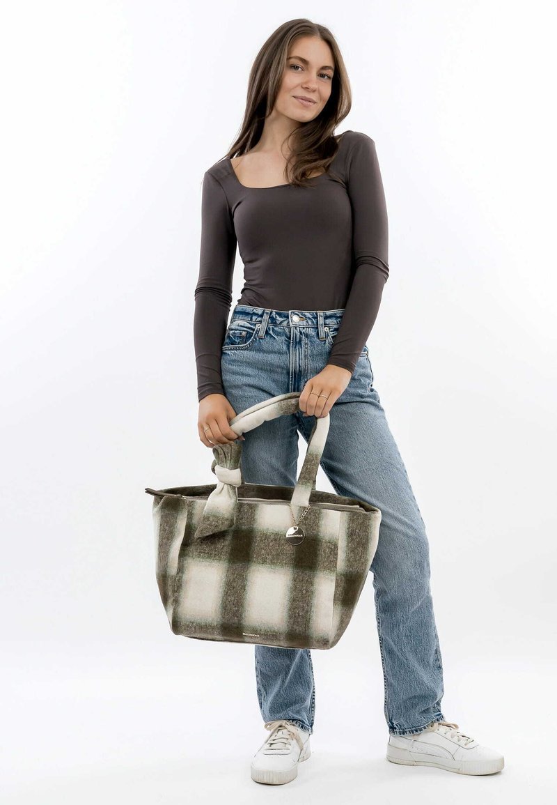 Khaki- und cremefarbene kariert Stofftasche mit zwei gebundenen Griffen, aus weichem Material. Modell trägt ein enges langärmliges Oberteil und helle Jeans.