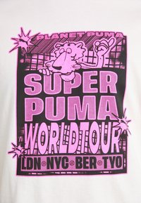 Balta T-kreklā ar grafisko dizainu rozā un melnās krāsās. Teksts ietver "PLANET PUMA", "SUPER PUMA" un "WORLDTOUR". Ievērojams multfilmu varonis.