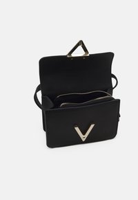 Borsa a tracolla in pelle nera con un accento in hardware dorato a forma triangolare e un logo a forma di V. L'interno presenta due scomparti con zip.
