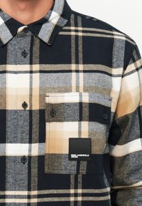 Camicia di flanella a quadri in navy, beige e bianco. Caratterizzata da bottoni, una tasca sul petto e un'etichetta del logo nero. Texture morbida.