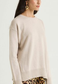 Beiger Strickpullover mit Rundhalsausschnitt, Rippensaum und überschnittenen Schultern. Kombiniert mit gemusterten Leopardenmuster-Hosen.