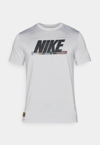 T-shirt Nike blanc à manches courtes avec un grand logo noir sur la poitrine, accompagné d'un motif graphique texturé derrière le logo.