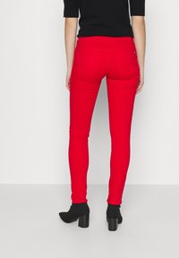 Jeans ajustados rojos con una textura suave, que cuentan con dos bolsillos traseros y una cinturilla de media altura. Combinados con botines negros con tacón.
