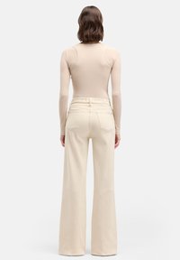 Beige geribbelde top met lange mouwen, gecombineerd met hooggetailleerde, brede broekspijpen in lichtcrèmekleur. De broek heeft twee achterzakken en een gladde textuur.