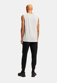 Hvid ærmeløs top med rund halsudskæring, detaljer på ryggen, parret med sorte joggers. Sorte atletiske sko fuldender outfittet.