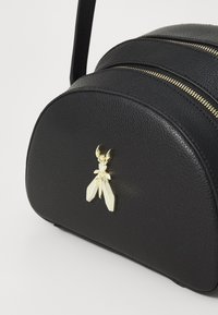 Borsa a mano in pelle nera con forma arrotondata, doppi zip dorati e un charm decorativo a forma di insetto in oro e cristallo.