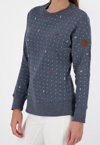 Szary sweter z białymi kotwicami i czerwonymi kropkami, z okrągłym dekoltem, ściągaczami przy mankietach i dole, z brązową skórzaną metką logo na rękawie.