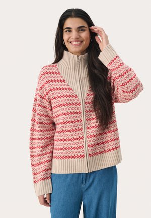Beige zip-up cardigan with a red geometric pattern, ribbed collar and cuffs, relaxed fit, paired with blue jeans.