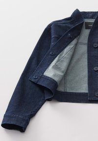 Veste en denim bleu foncé avec un extérieur texturé et une doublure plus claire. Présente des boutons contrastants et un design court avec des coutures ajustées.