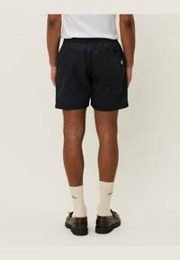 Svart, teksturerte shorts med elastisk midje, sidelommer og baklomme. Brukt med kremfargede sokker og brune sko.