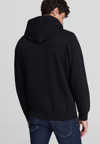 Felpa nera con cappuccio realizzata in tessuto morbido, caratterizzata da una vestibilità rilassata, polsini e orlo ribattuti. Dettagli di cucitura discreti arricchiscono il design.