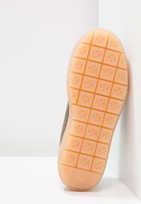 Schuhsohle in hellorange mit geprägtem Quadratmuster. Obermaterial aus olivgrünem Stoff, strukturiert und flaches Design.