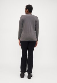 Grå långärmad topp i kombination med svarta utsvängda byxor och kraftiga svarta skor. Slät struktur, enkel design och åtsittande siluett.