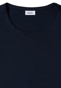 T-shirt bleu marine à col rond avec une étiquette de marque rectangulaire blanche « CECIL » cousue à l'intérieur de l'encolure arrière.