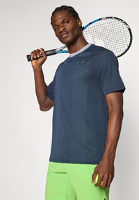 Camiseta atlética de color marino con mangas cortas, tejido texturizado y acentos en azul claro cerca del cuello, combinada con pantalones cortos de color verde brillante.