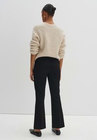 Pull en maille beige avec un motif texturé, associé à un pantalon tailleur noir et des ballerines noires, vu de dos.