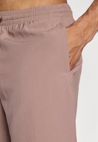 Støvete rosa treningsshorts med elastisk midjebånd, sidelomme, glatt tekstur og avslappet passform. Sømdetaljer er synlige.